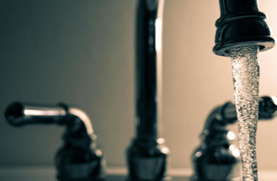 Water flowing from a kitchen faucet into a sink, with blurred taps in the background