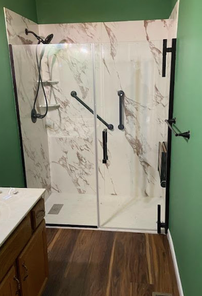 Modern bathroom shower with marble-pattern tile, black hardware, and a glass door beside a vanity
