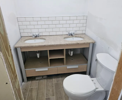 Small bathroom with double sink vanity and toilet, white subway tile backsplash, and beige floor tiles