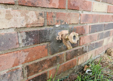 Close-up of a brick wall with a metal outdoor water faucet and spigot.