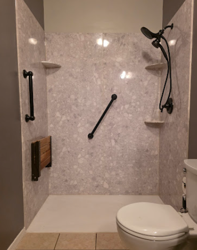 Accessible shower with grab bars, built-in shelves, handheld showerhead, and toilet in a tiled bathroom.