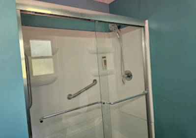 Glass shower stall with chrome grab bar and white-tiled bathroom walls