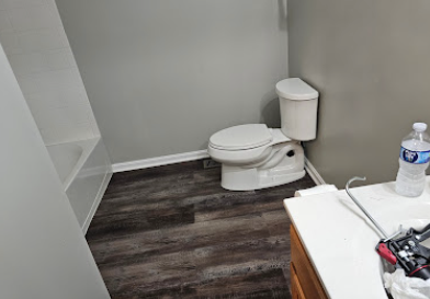 Small bathroom with a toilet, dark wood floor, and a sink counter with toiletries.