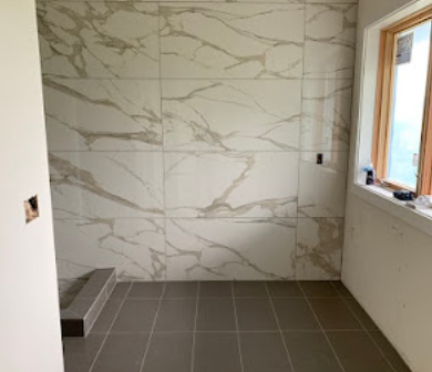 Empty tiled shower with marble-look wall panels, a small step, and a window on the right.
