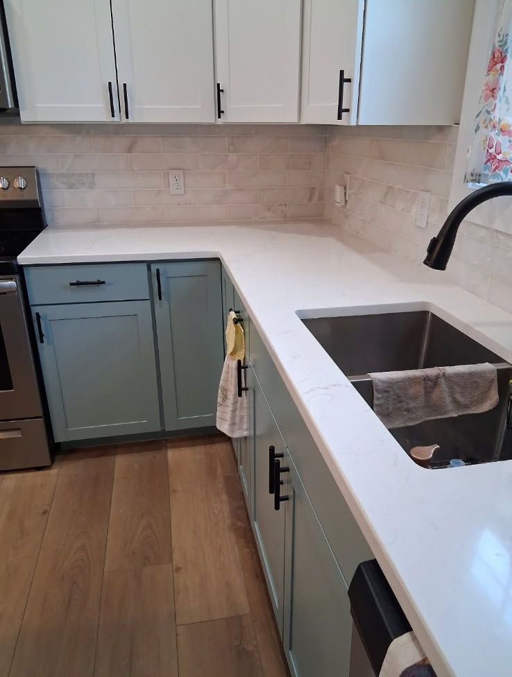 Modern kitchen with white countertops, blue lower cabinets, wood floor, and a double-basin sink by a black faucet