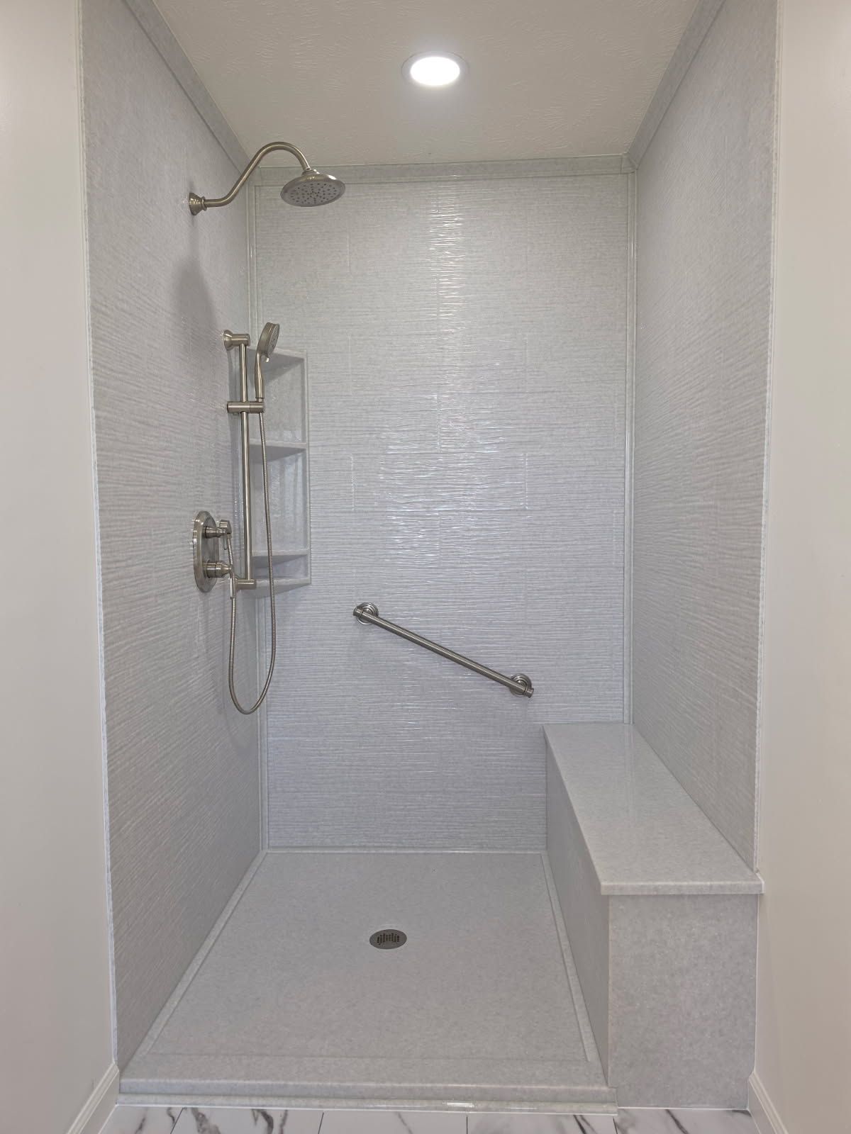 Accessible shower stall with handheld showerhead, built-in bench, and grab bar in a tiled bathroom