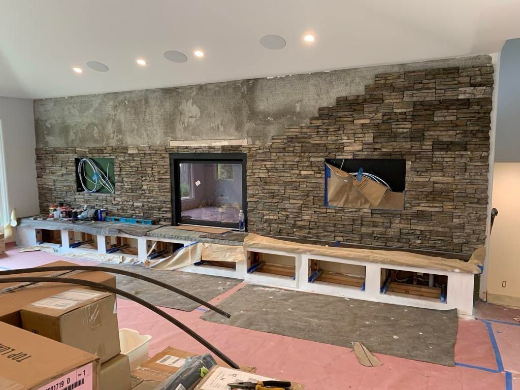Living room with stone accent wall, TV and fireplace opening, under renovation with boxes and blue tape