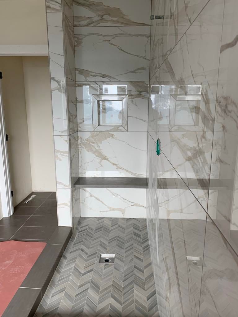 Modern tiled bathroom shower area with glass partition and wall niche, viewed from the doorway