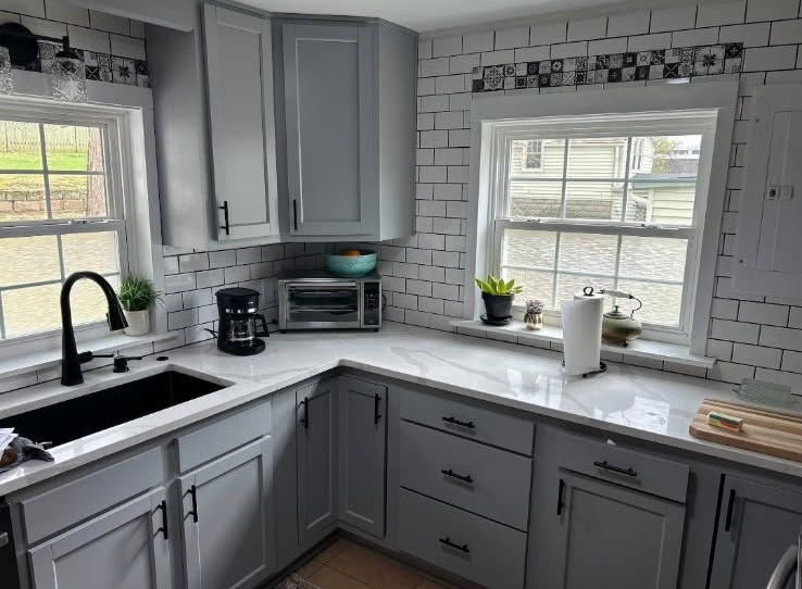 Gray kitchen with white tile backsplash, countertops, and gray cabinets. Black sink and appliances.