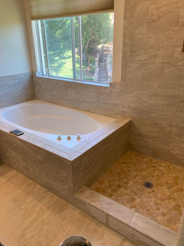 Bathroom with a built-in soaking tub, tiled shower, and window overlooking greenery.