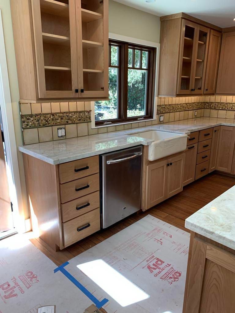 Bright kitchen with wooden cabinets, white countertop, stainless dishwasher, and a sink by a window under construction.