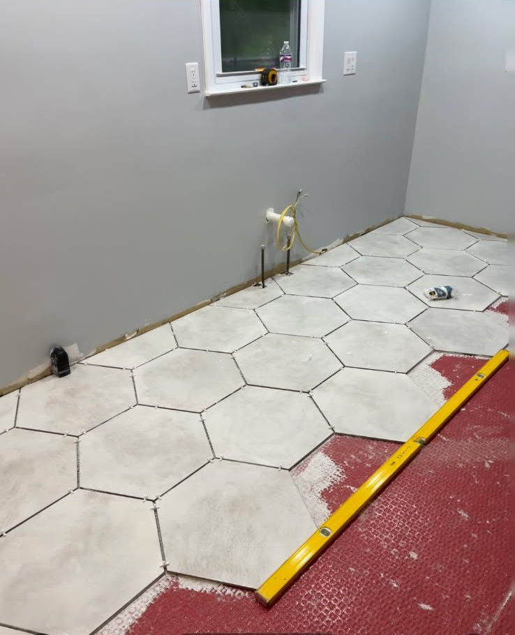 Hexagon tile flooring being installed in a room with gray walls. A level lies on the red underlayment.