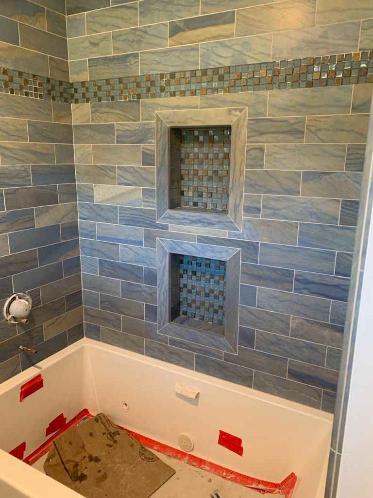 Tiled shower niche wall with two recessed shelves and a white tub below, under construction