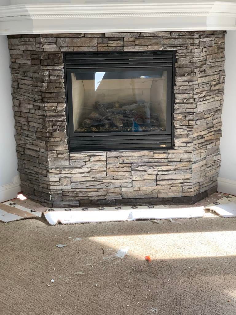 Stone fireplace with a black glass insert in a living room, surrounded by carpet and white trim.