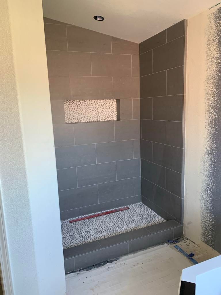 Small gray-tiled shower stall with a built-in bench and mosaic tile accents.