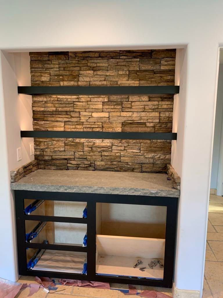 Built-in wall niche with stone backsplash, dark shelves, and unfinished lower cabinetry.