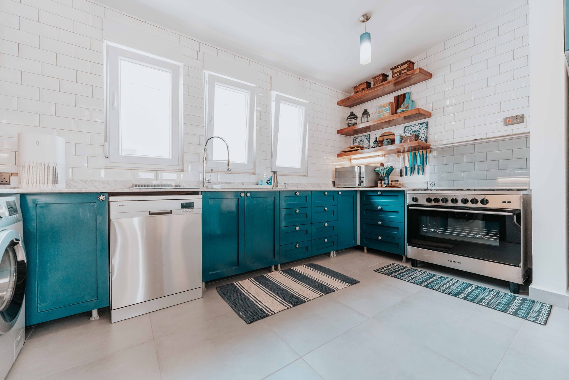 Bright white kitchen with teal lower cabinets, farmhouse sink, open shelves, and a stainless oven.