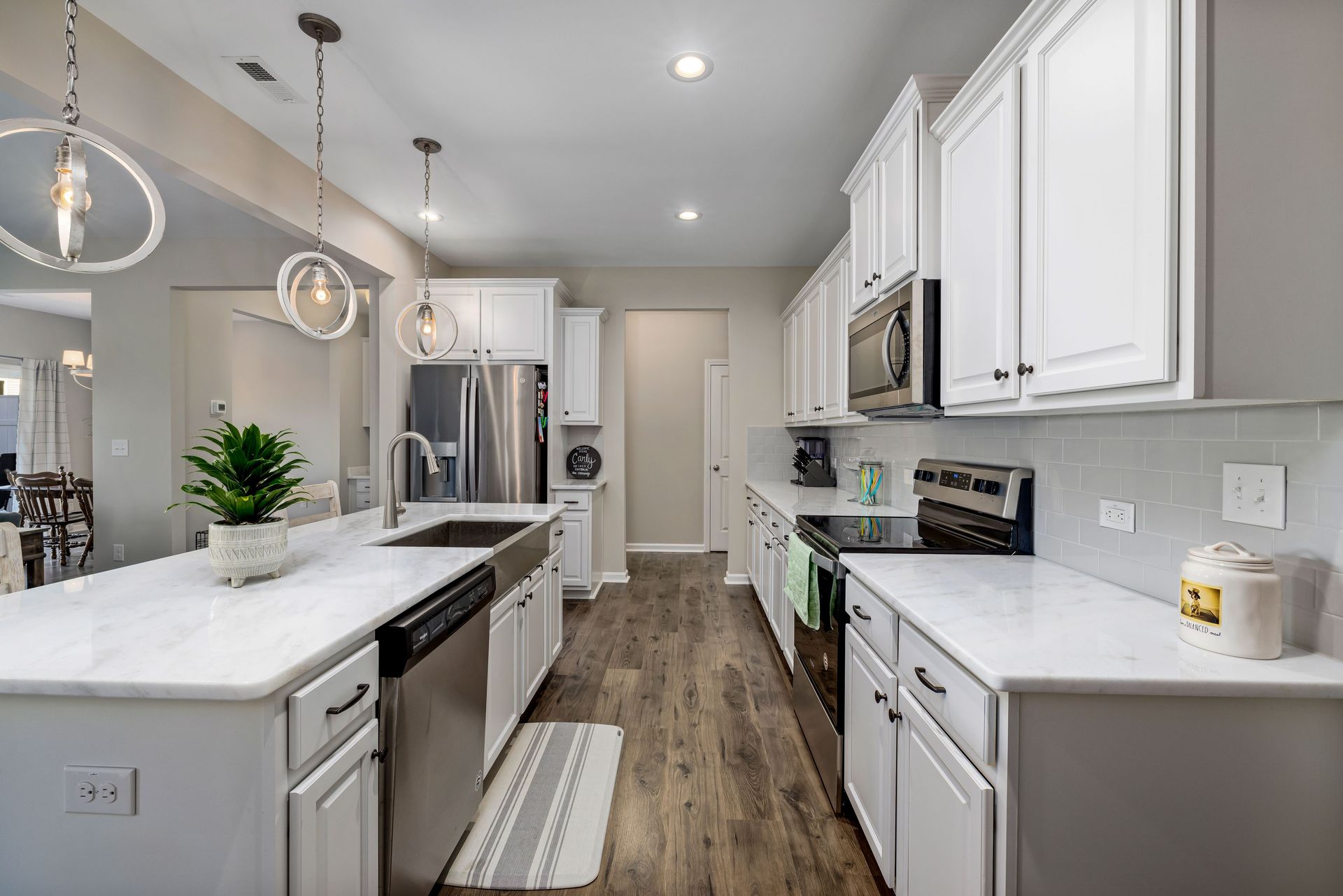Bright modern white kitchen with stainless steel appliances, island, and wood-look flooring