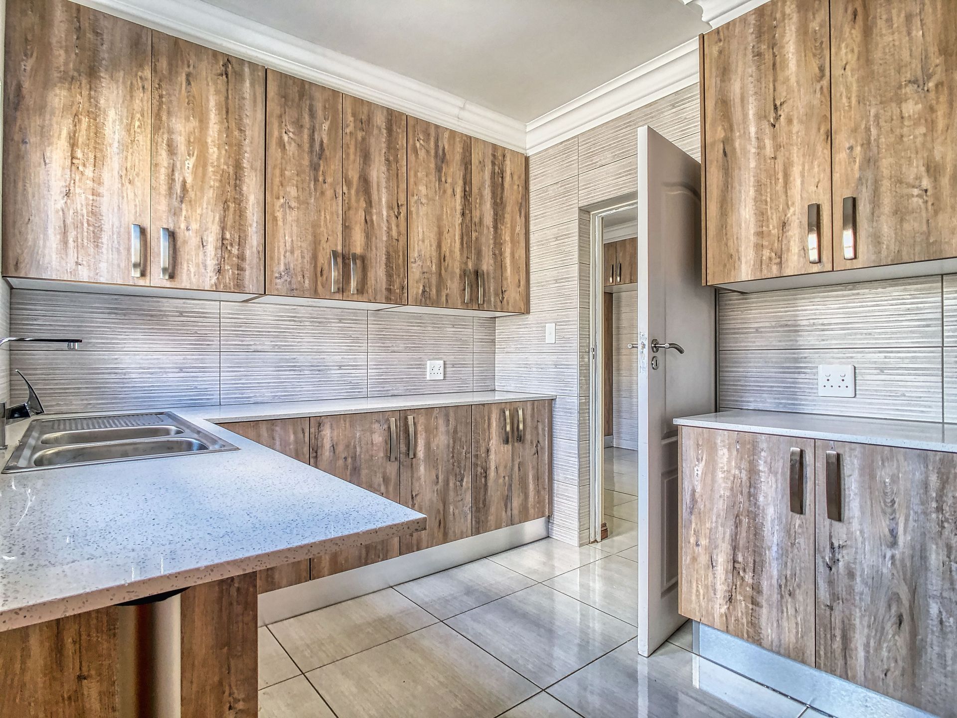Empty kitchen with wood-grain cabinets, light tile floor, and a speckled countertop.
