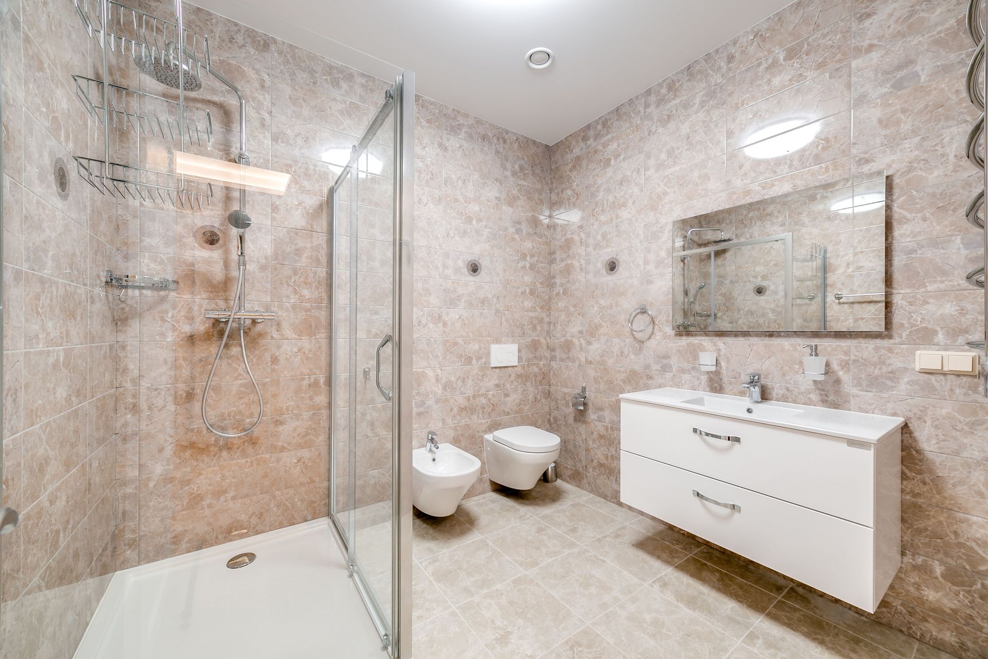Modern beige bathroom with glass shower, toilet, and white vanity with mirror