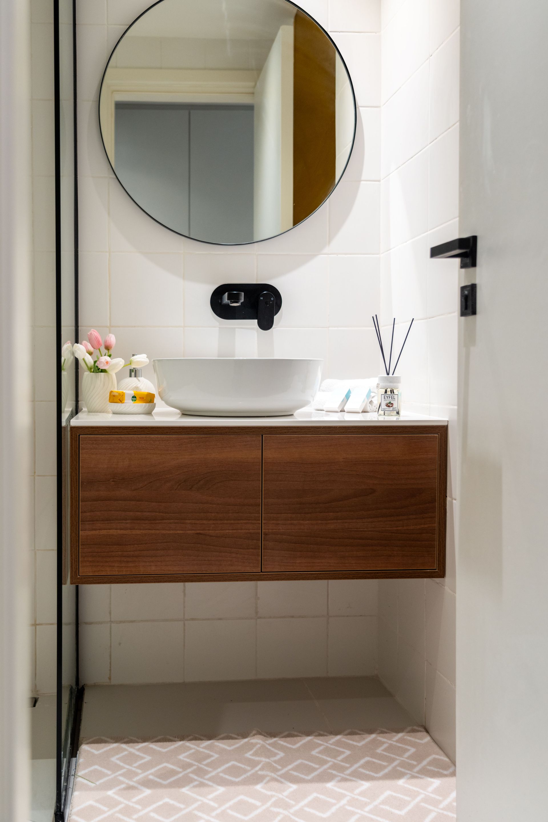 Modern bathroom vanity with round mirror, white sink, and wood cabinet in a tiled nook