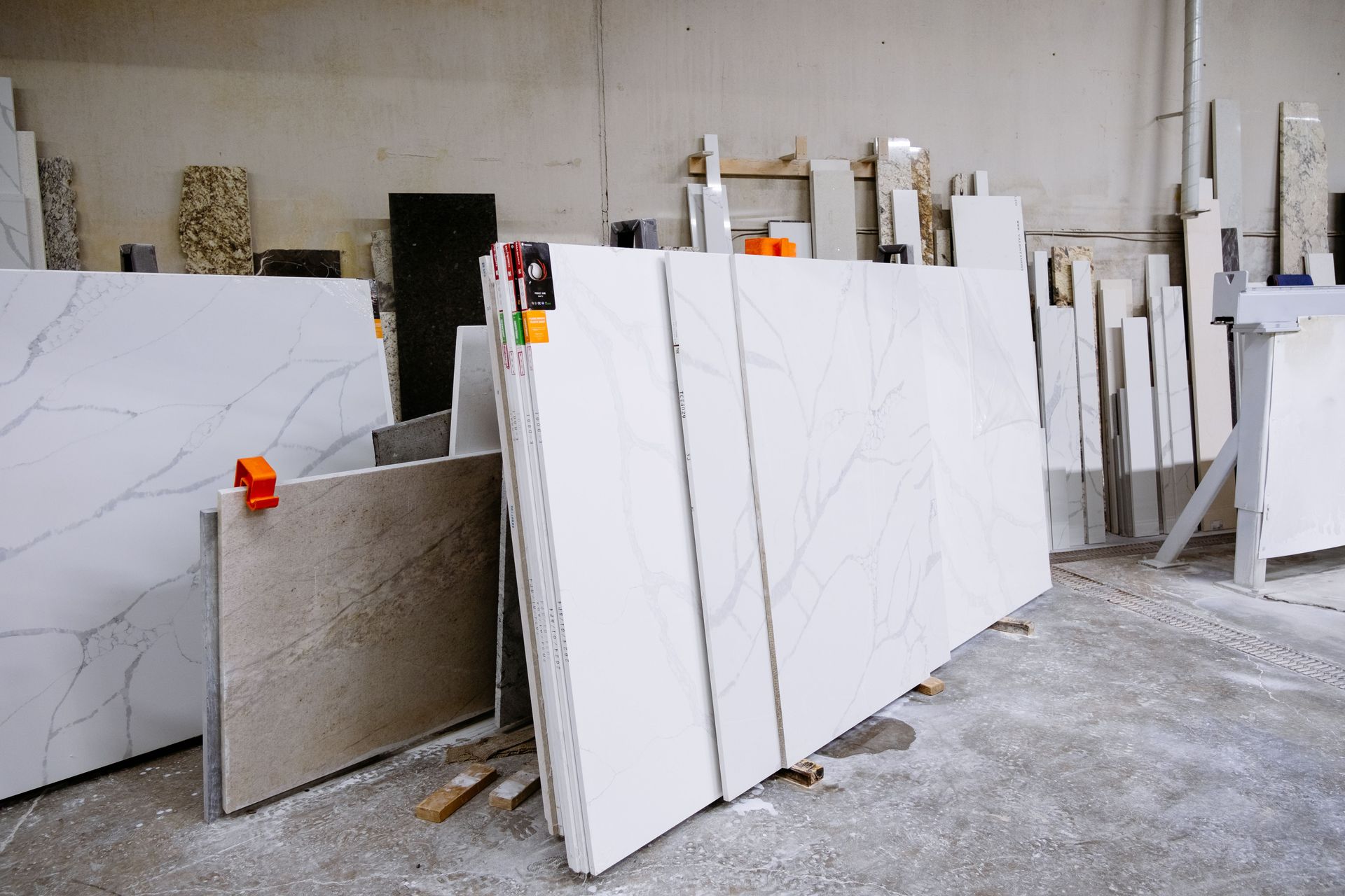 Marble slabs stacked in a stone warehouse, with white and gray slabs leaning on stands.