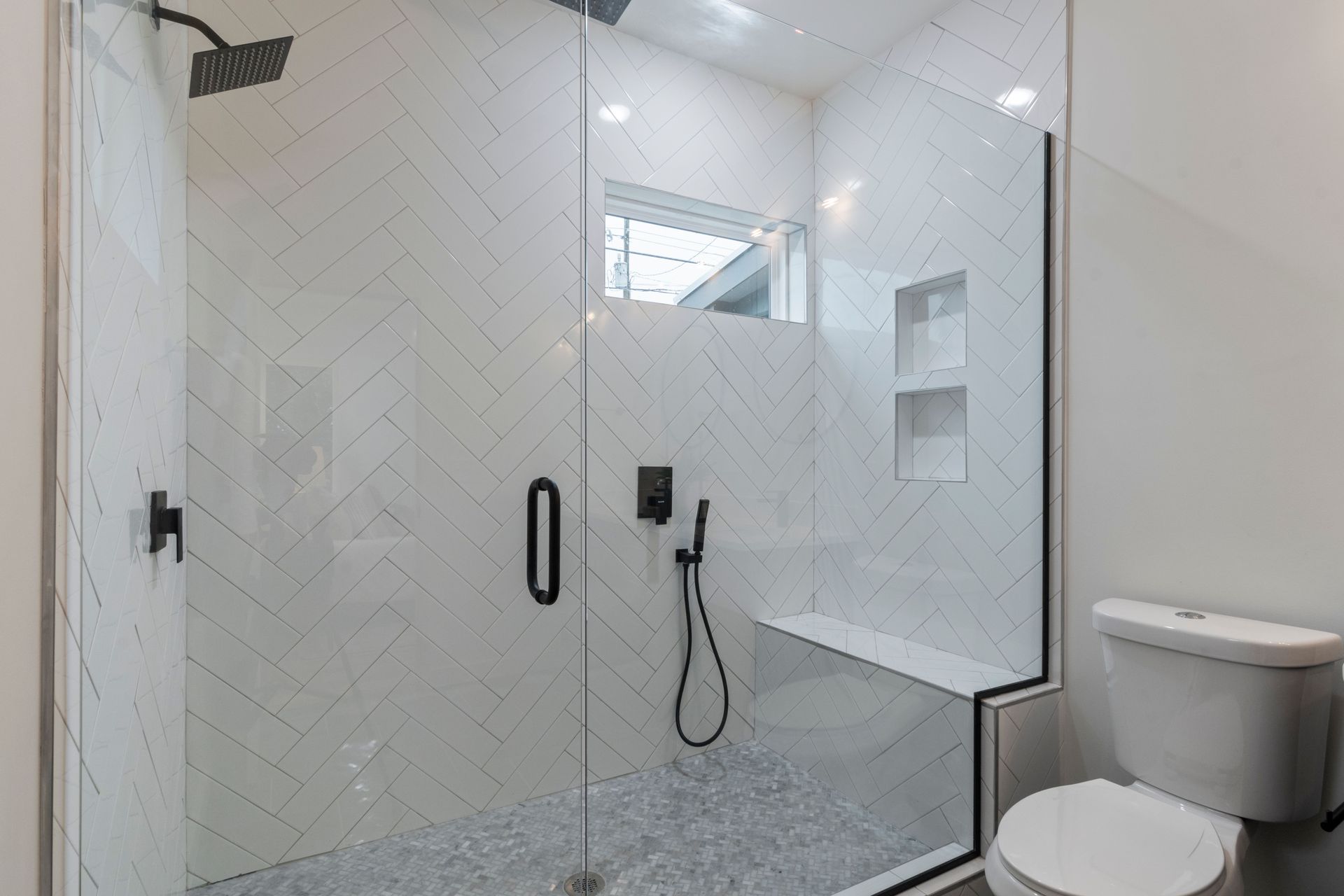 Modern white bathroom with a glass shower enclosure, built-in shelves, and a toilet