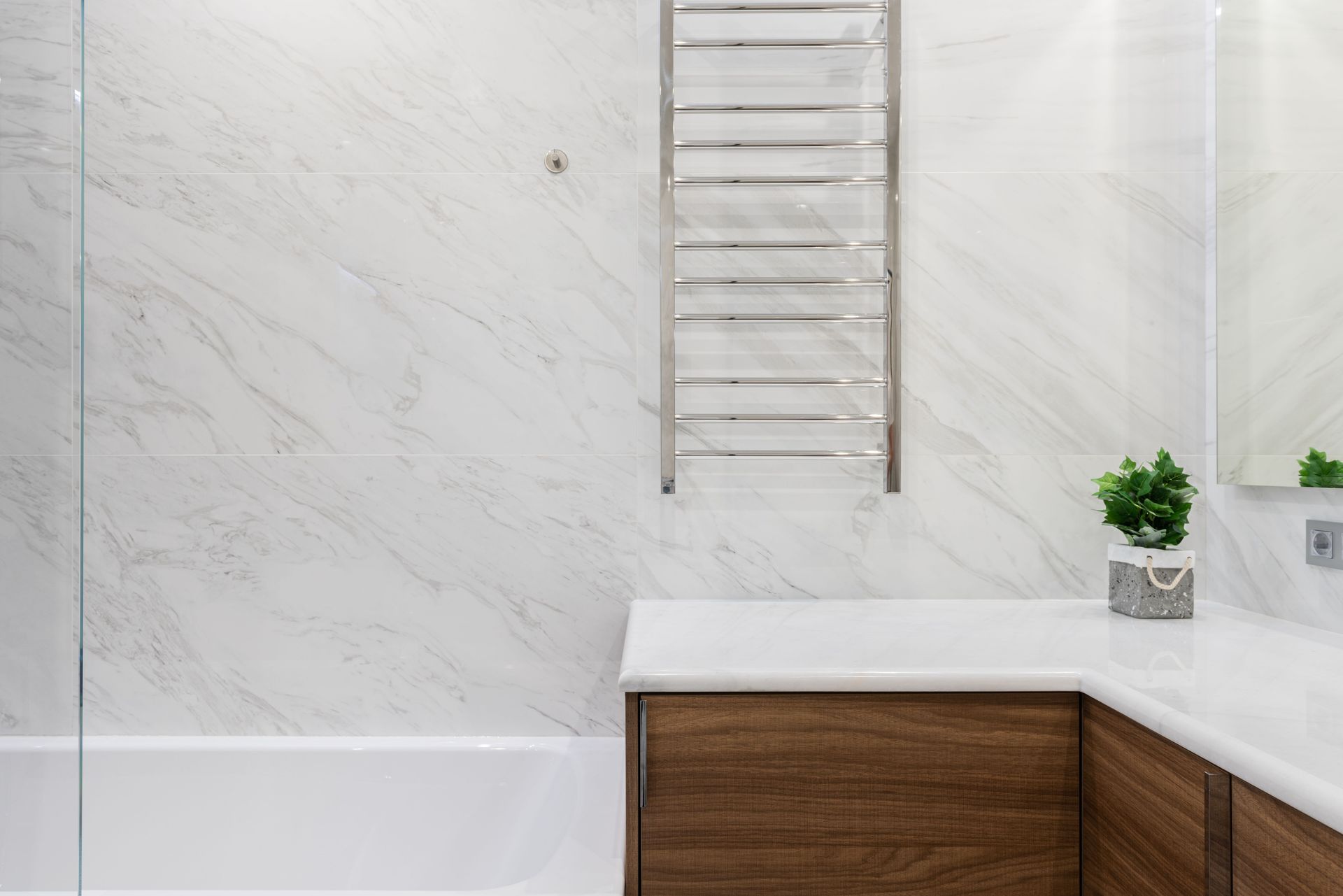 Modern bathroom with white marble walls, wood vanity, towel rack, and a small potted plant.