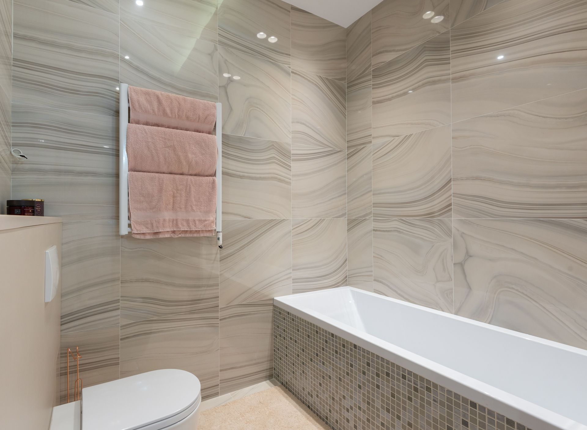 Modern bathroom with marble-look walls, a white tub, and a pink towel rack.