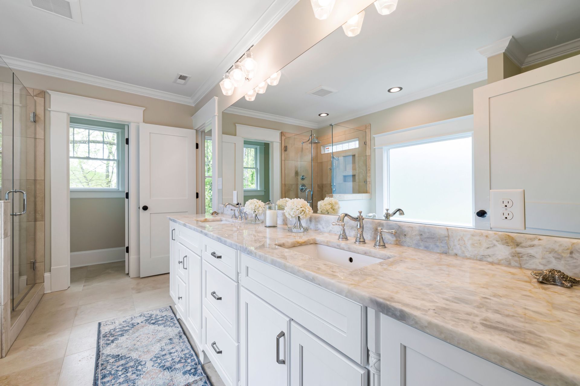 Bright bathroom vanity with marble countertop, double sinks, large mirror, and soft white cabinetry