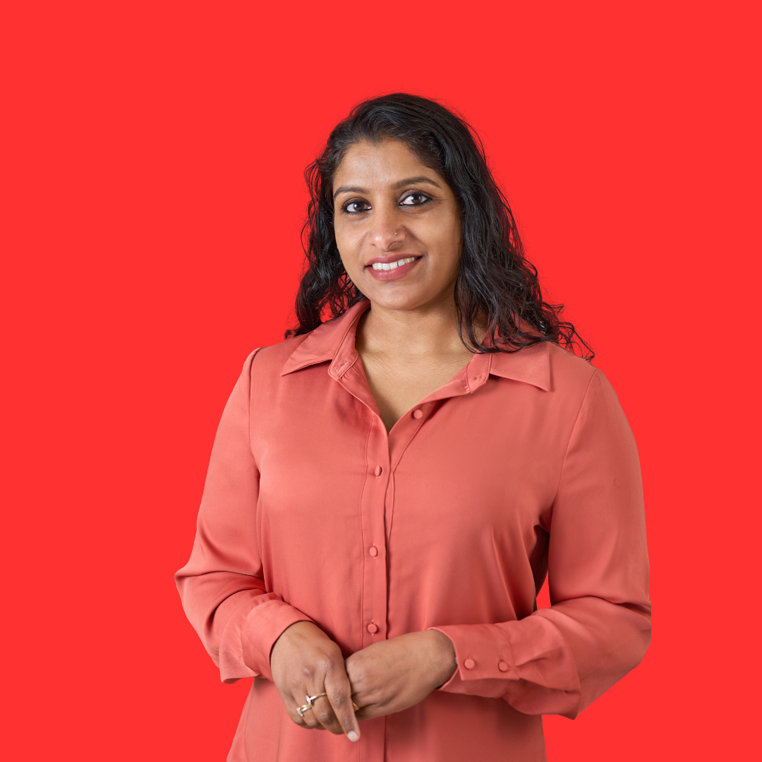 A woman in a red shirt is standing in front of a red background.