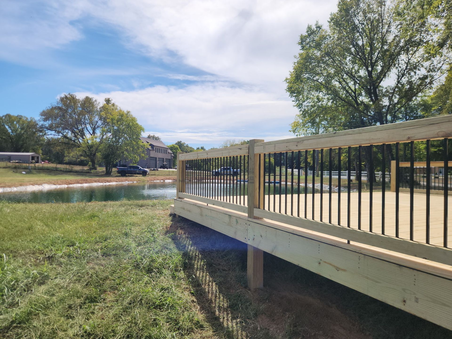 Footbridge over a grassy creek with trees and homes under a partly cloudy sky