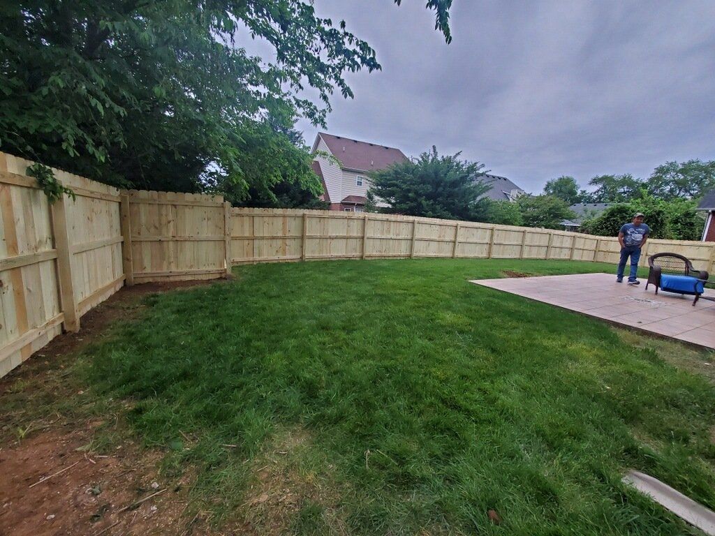 A man is standing in a backyard next to a wooden fence.