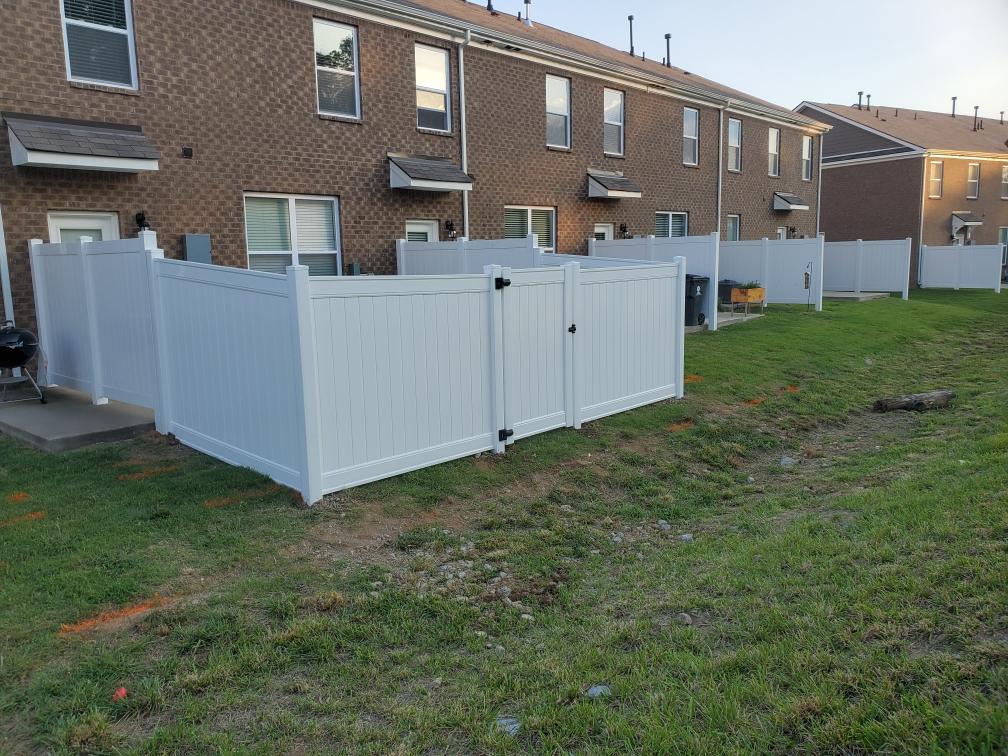 A white fence is in the middle of a grassy field in front of a brick building.