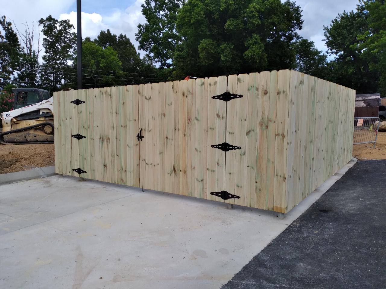 A wooden fence with black hinges is in a parking lot.
