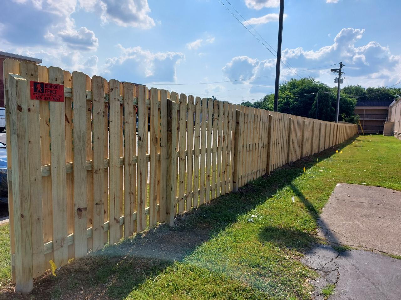 A wooden fence is sitting on the side of the road next to a sidewalk.