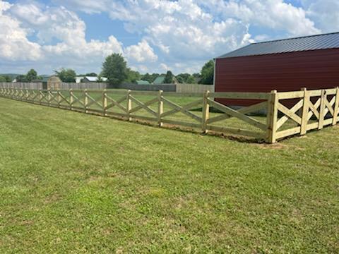 A wooden fence surrounds a grassy field with a red barn in the background.