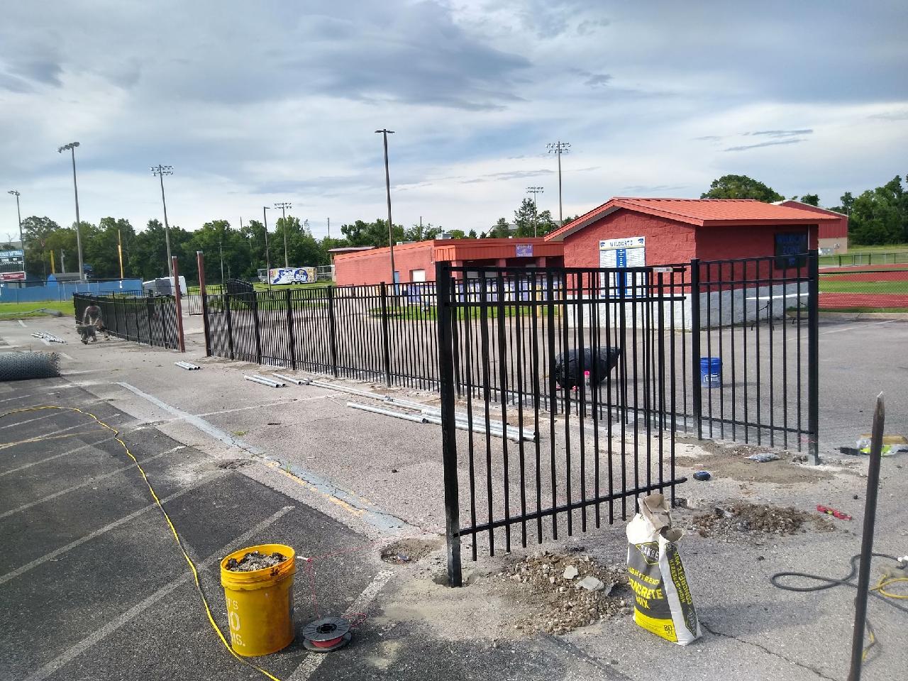 A yellow bucket is sitting on the sidewalk next to a metal fence.