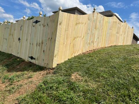 A wooden fence is sitting on top of a grassy hill next to a house.