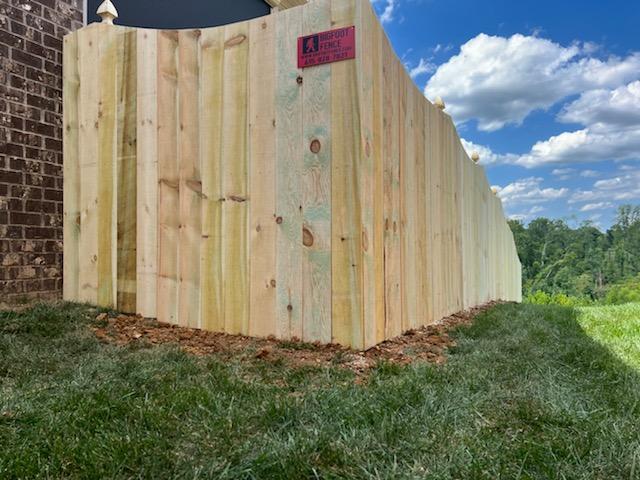 A wooden fence is sitting in the grass next to a brick building.