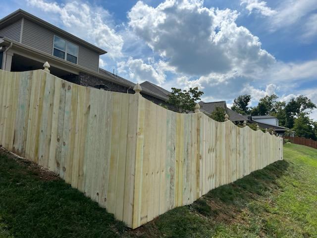 A wooden fence is sitting on top of a grassy hill next to a house.