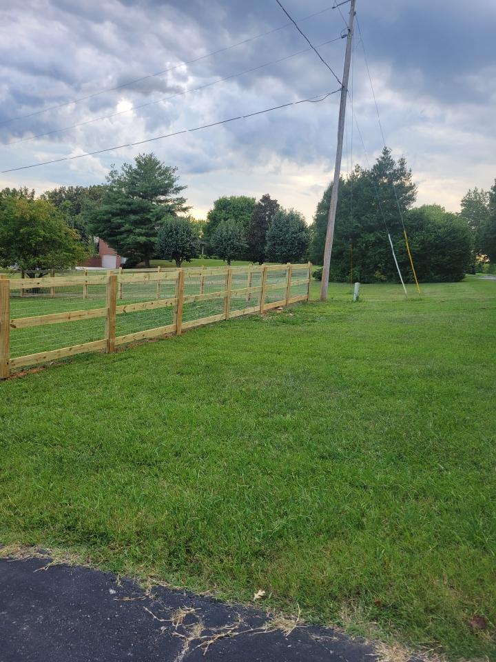 A wooden fence surrounds a lush green field.