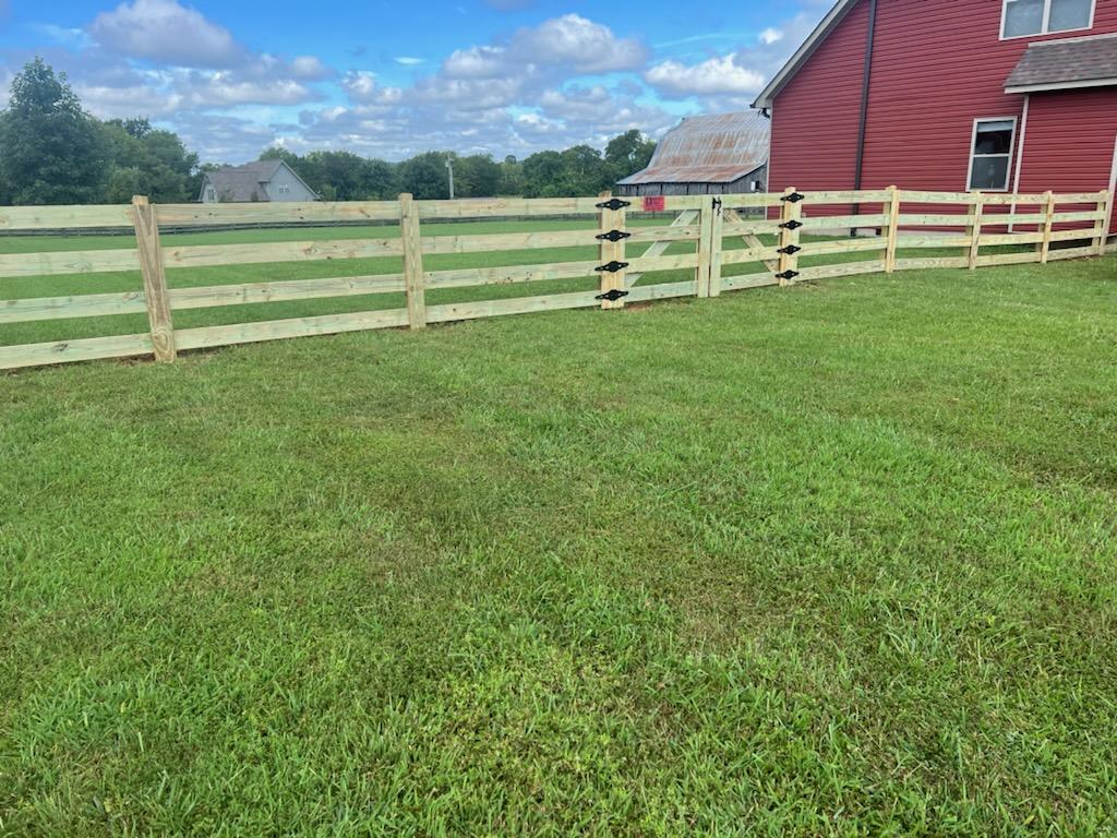 A wooden fence surrounds a lush green field in front of a red house.