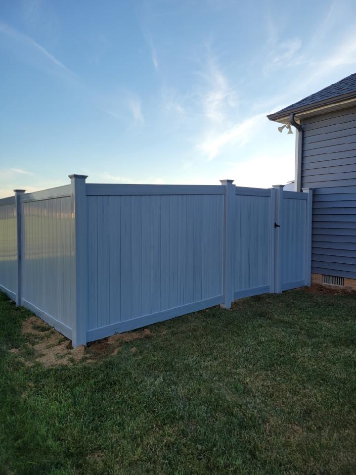 A white vinyl fence with a gate in the backyard of a house.