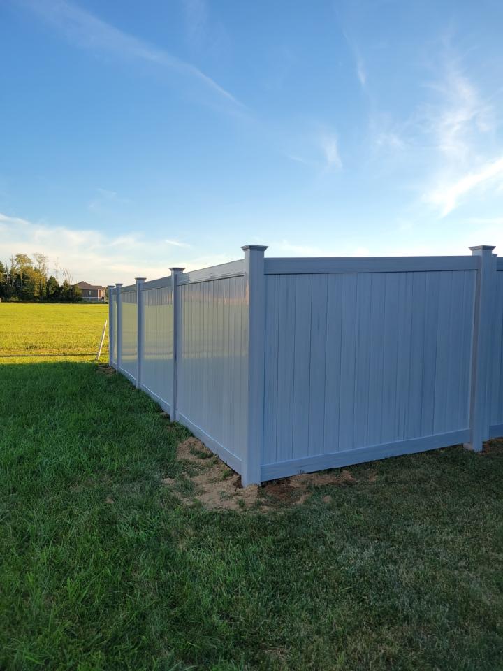 A white vinyl fence is sitting in the middle of a lush green field.