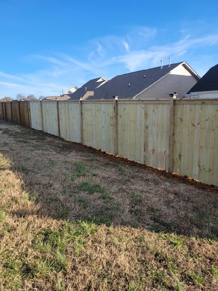 A wooden fence surrounds a grassy field in front of a house.