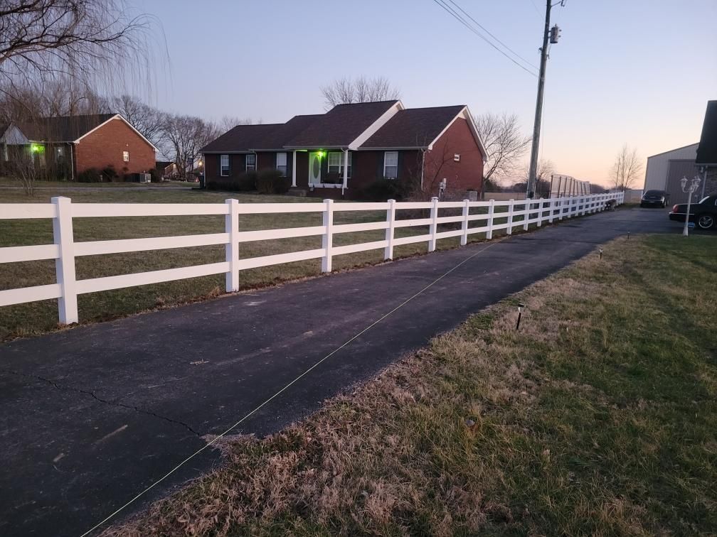 A white fence is along the side of a road in front of a house.