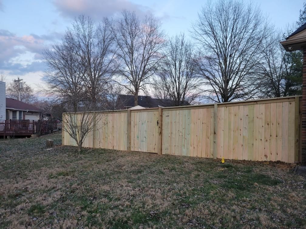 A wooden fence in a backyard with trees in the background.