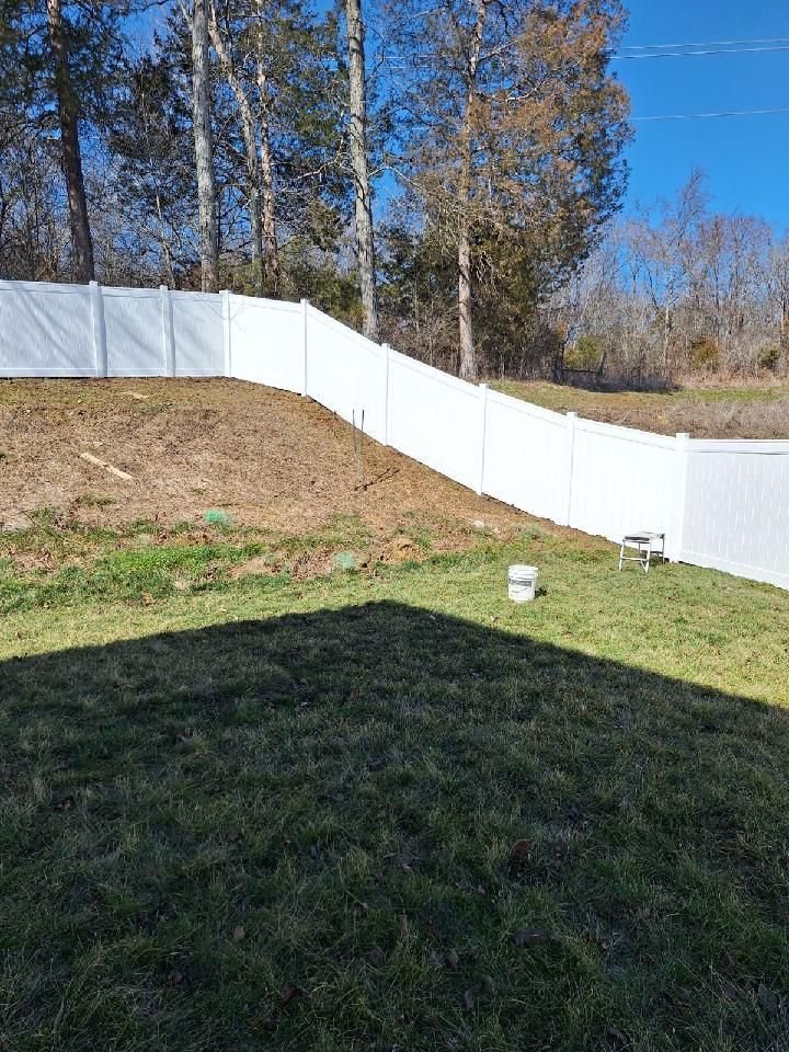 A white fence surrounds a lush green yard with trees in the background.
