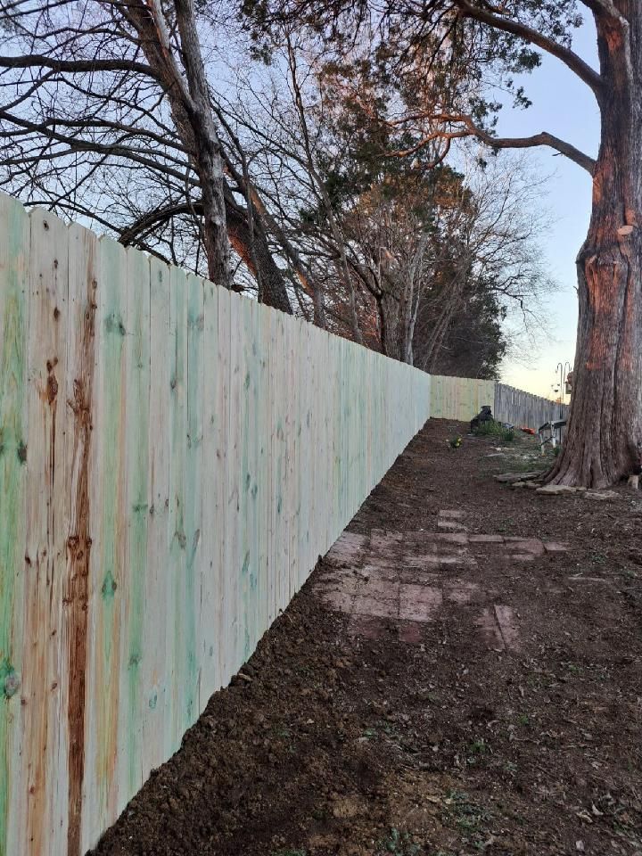 A wooden fence is surrounded by trees and dirt in a yard.